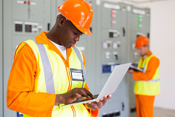 Black Technical Worker Using Laptop With Colleague On Background